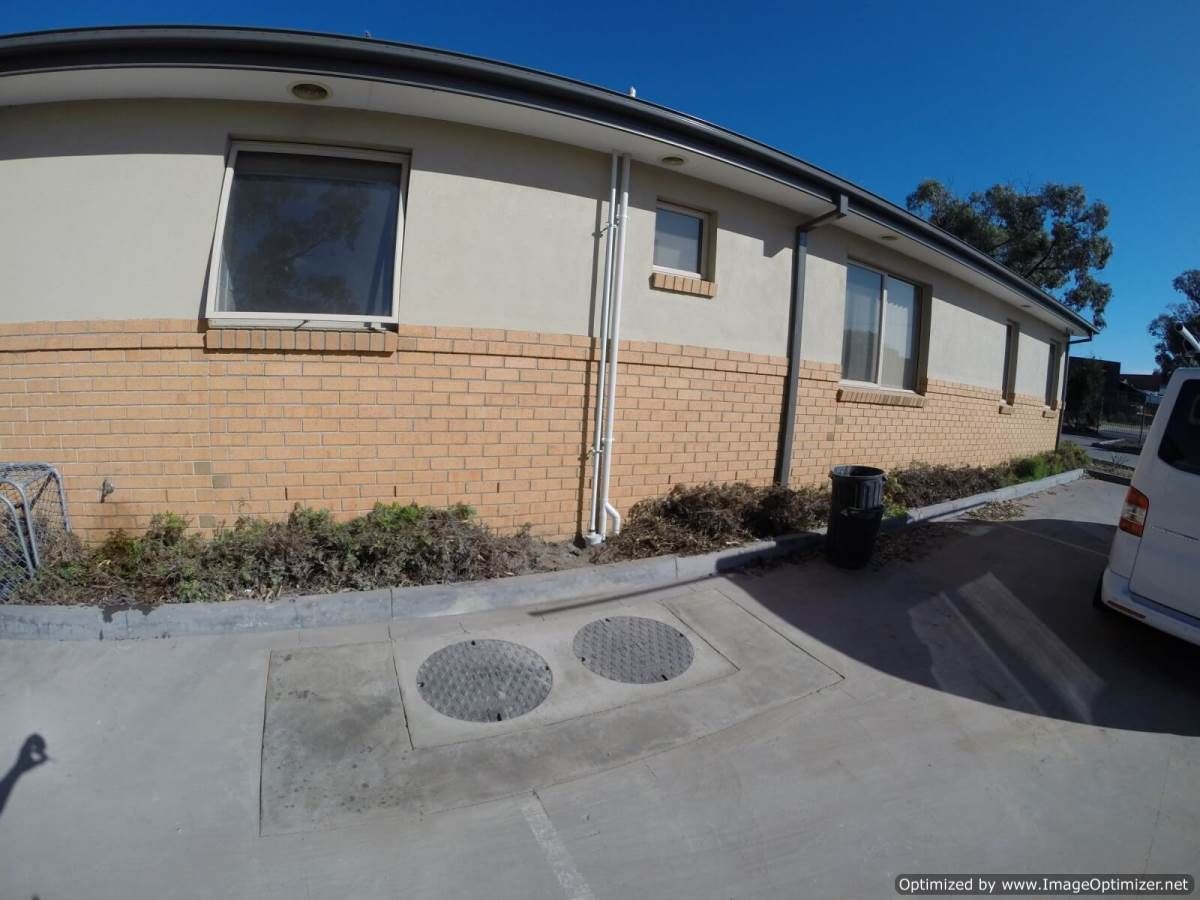 Building exterior with brick facade, windows, drain covers, and a parked van under a blue sky.