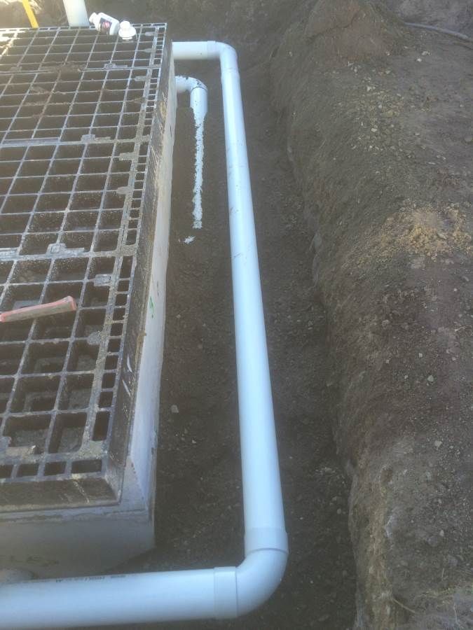 White PVC pipe installed in a trench next to a square grate.