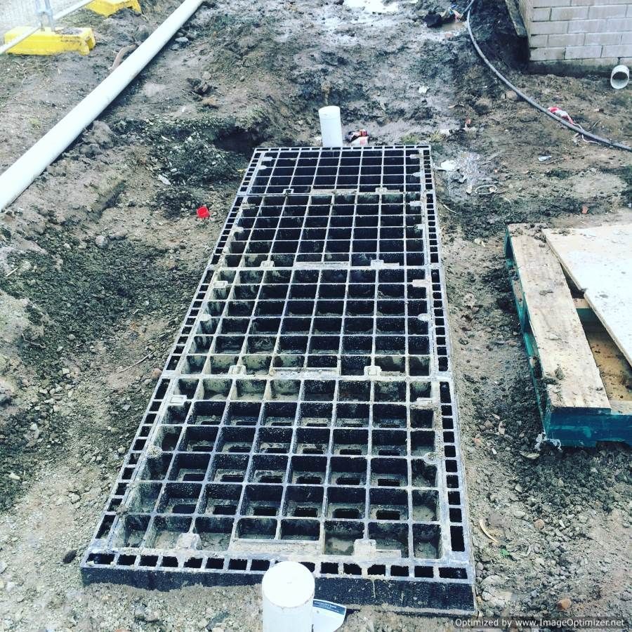 Metal grate installed in construction site. White PVC pipes and dirt surround the rectangular structure.