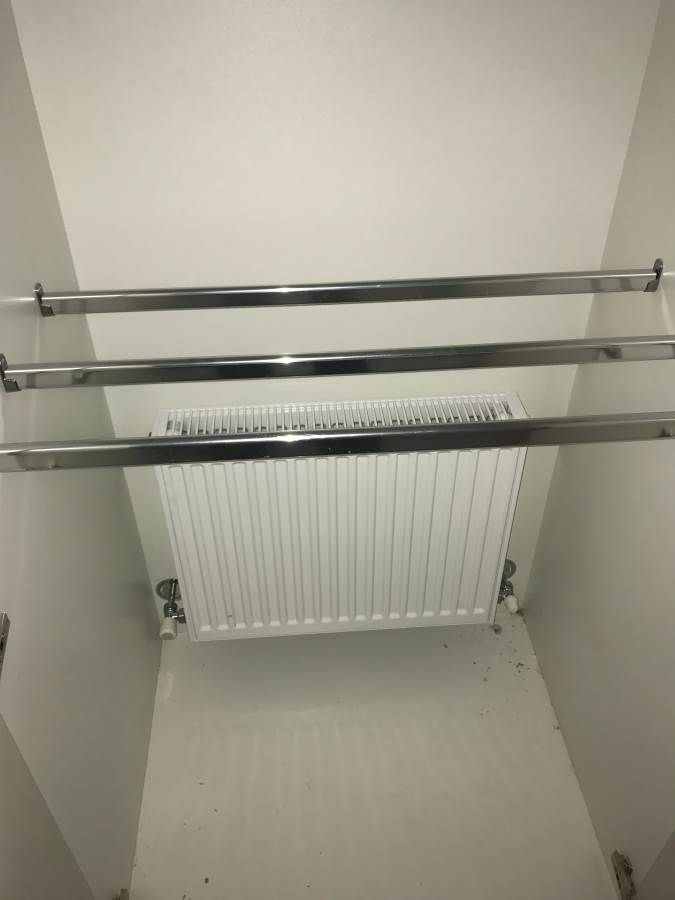 White closet with a radiator and three chrome clothing rods.