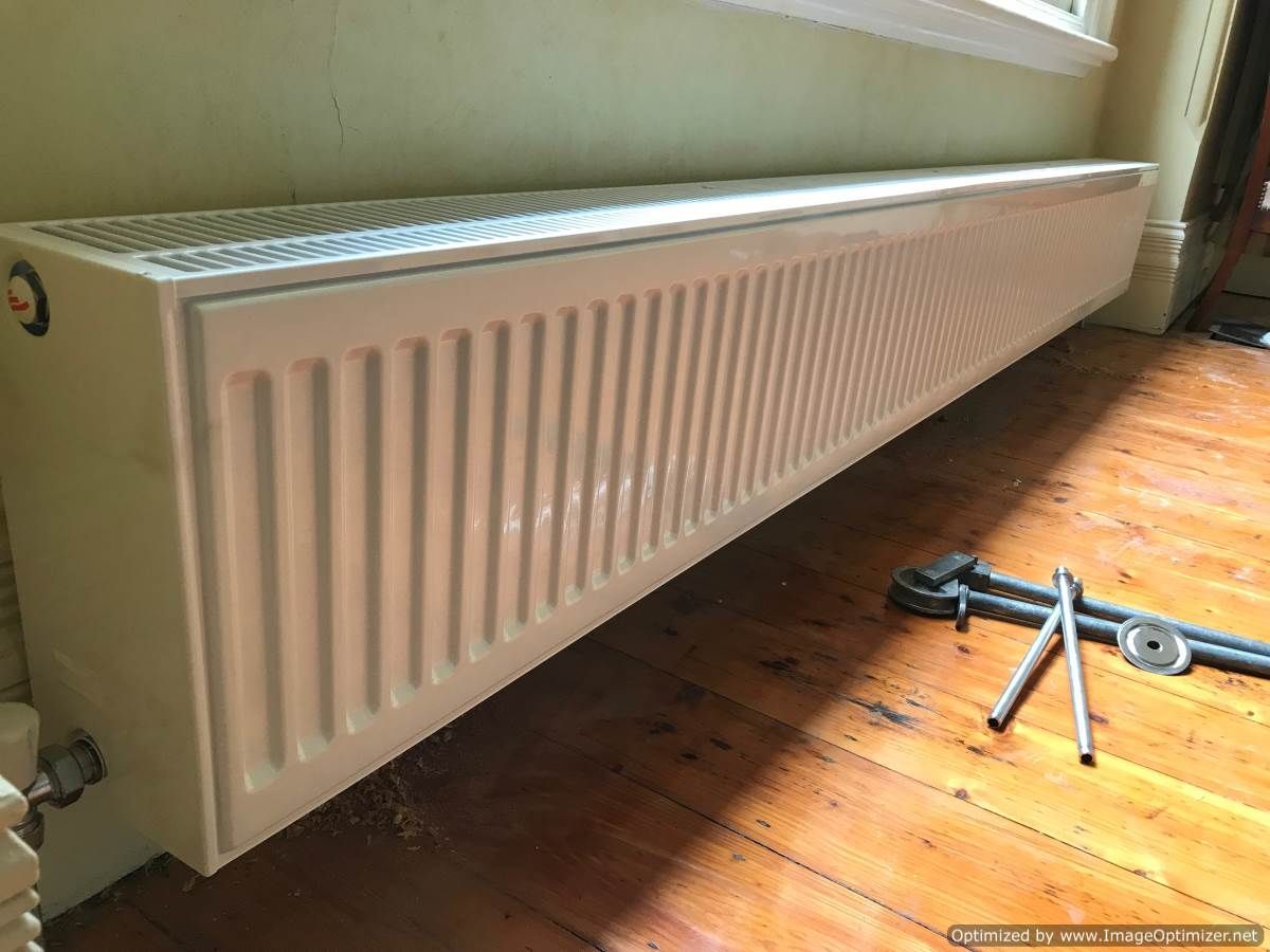 Long, white baseboard radiator on a hardwood floor, next to a window.