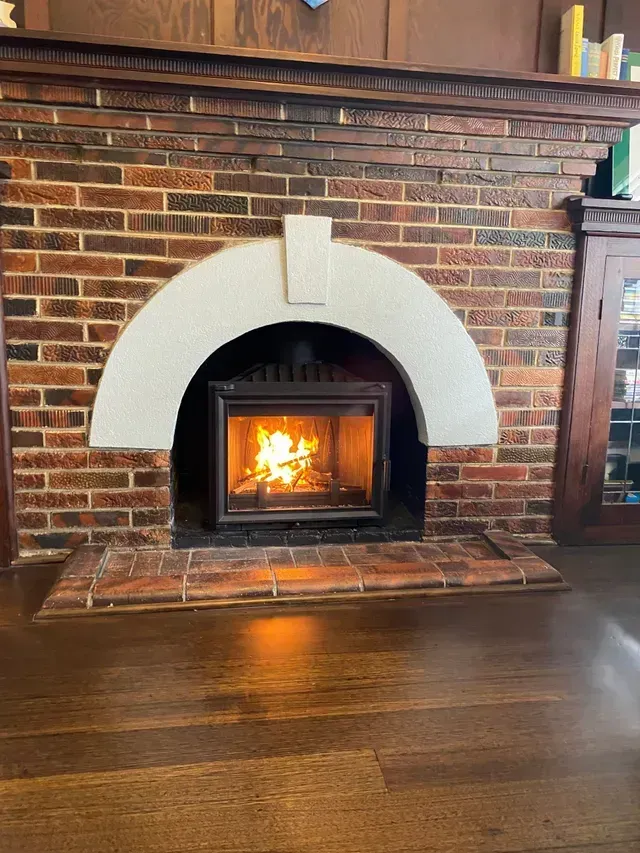 Brick fireplace with a burning fire, arched opening, and granite surround.