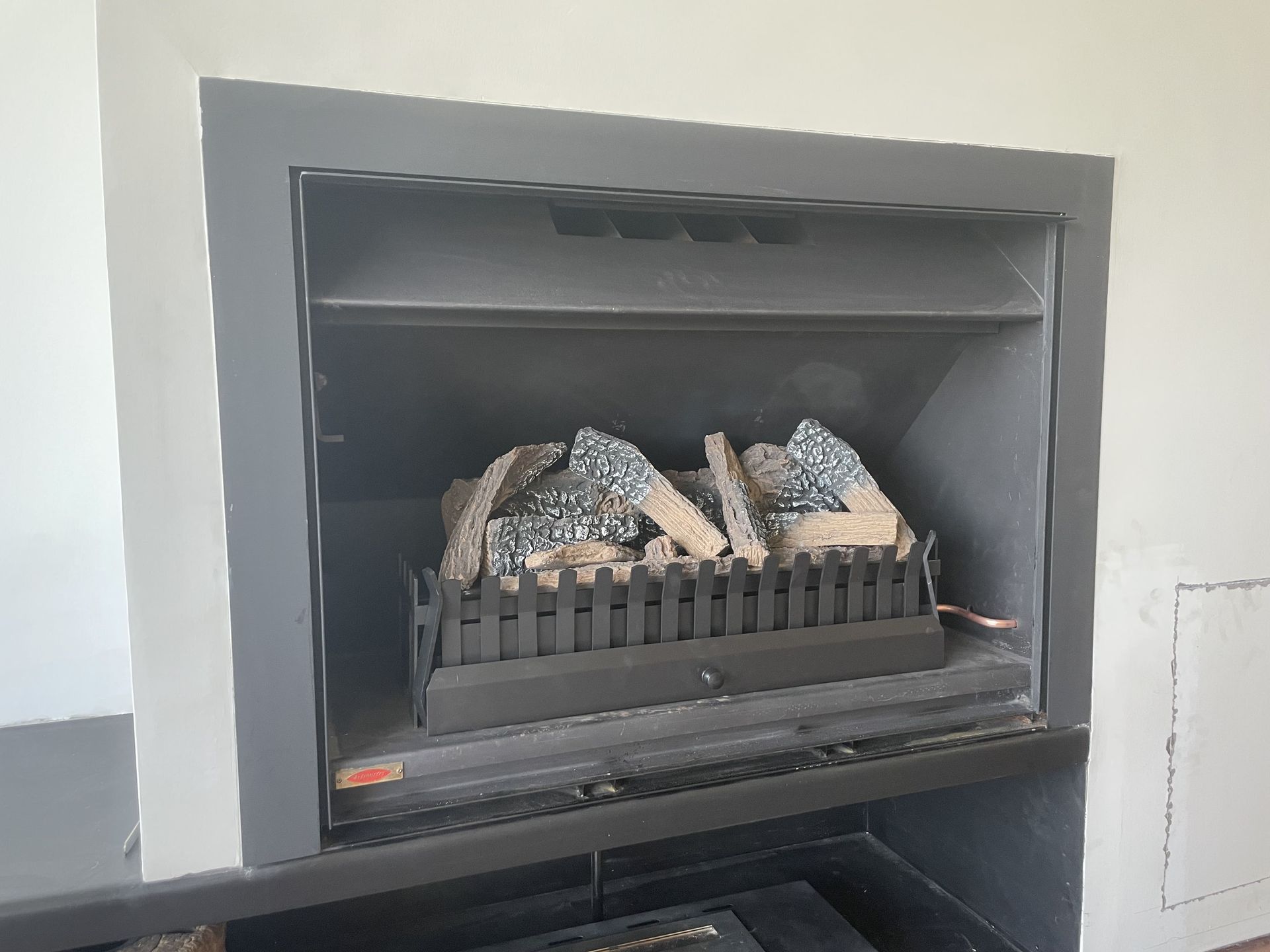 Black fireplace with faux logs and a black metal grate, set in a white wall.