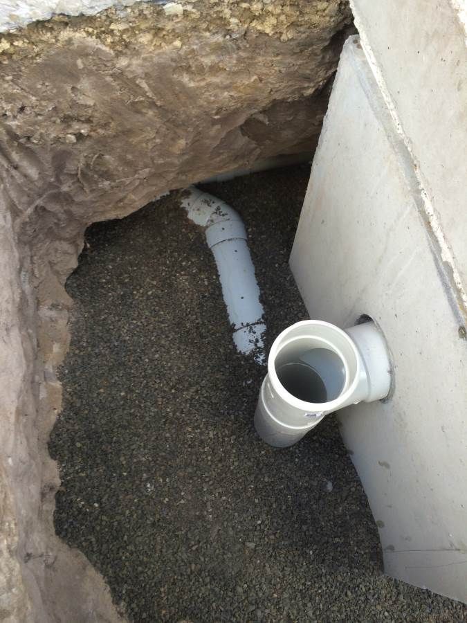 Grey pipes in a gravel-filled trench next to a concrete structure.