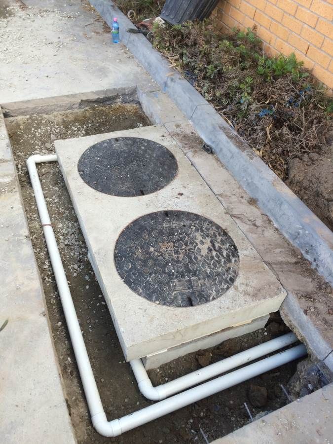 Concrete rectangular cover with two circular access points; white pipes run beneath.
