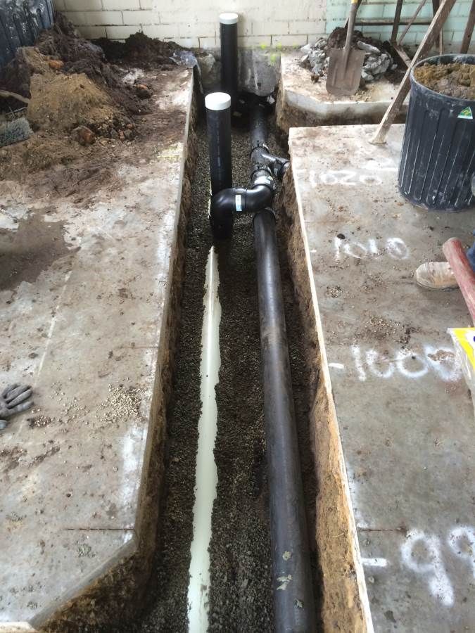 Trench with plumbing pipes laid inside. The pipes are black and white, running along the dirt.