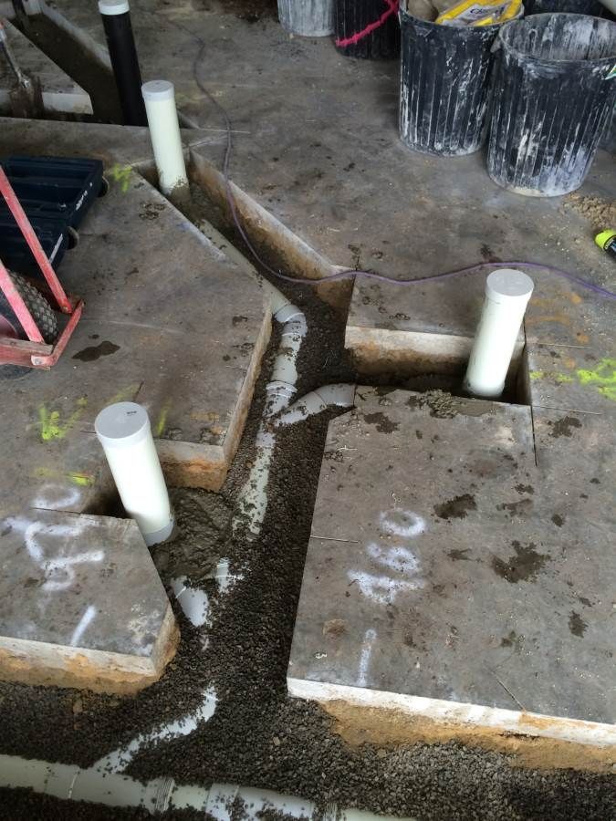Concrete floor with plumbing pipes and trenches filled with gravel.
