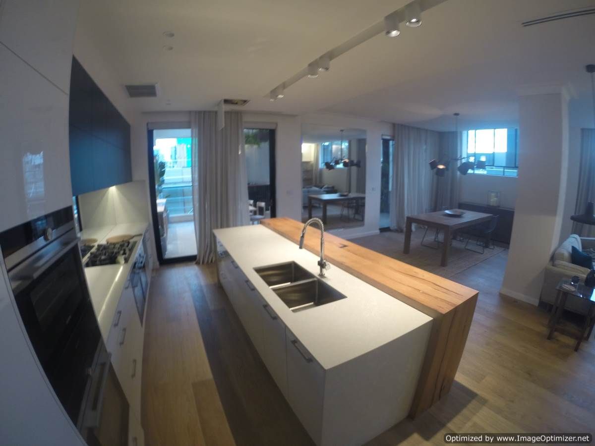 Modern kitchen with island, white cabinetry, wooden accents, and a view into a living space.