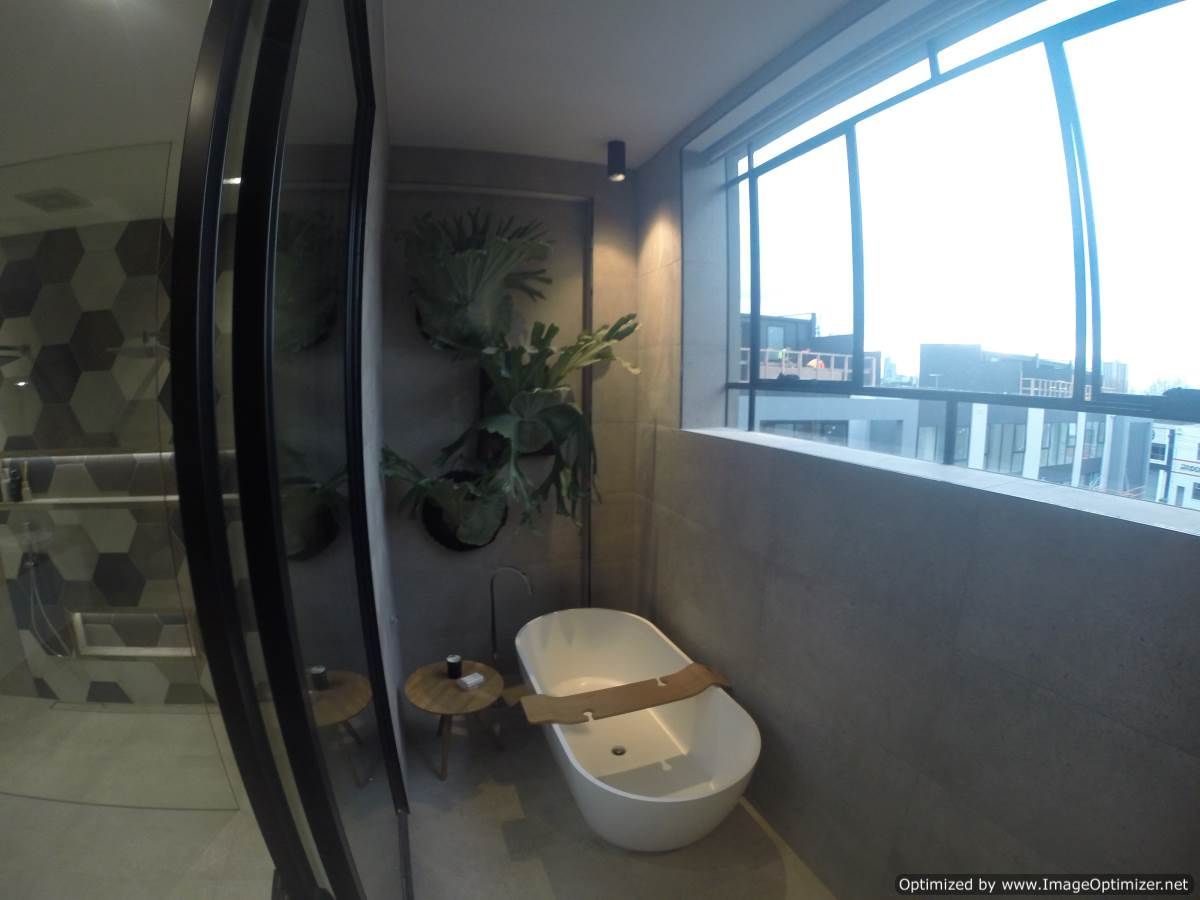 Modern bathroom with white tub, large window, and gray walls, plants.