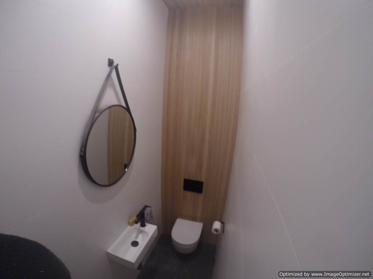 Small bathroom with a toilet, sink, mirror, and wood paneling on the wall.