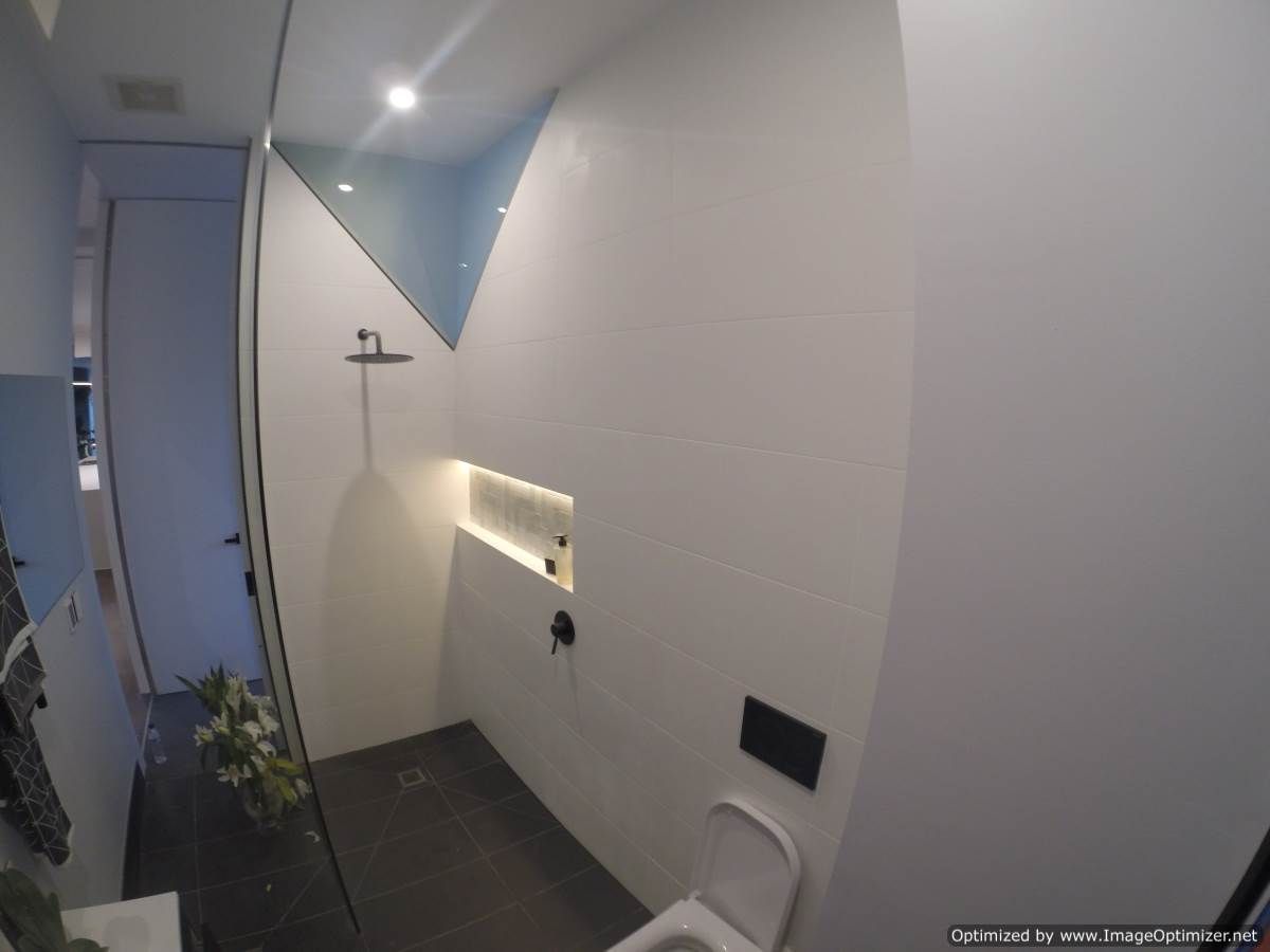 Modern white bathroom with shower and toilet, dark tile floor, and a geometric blue accent.