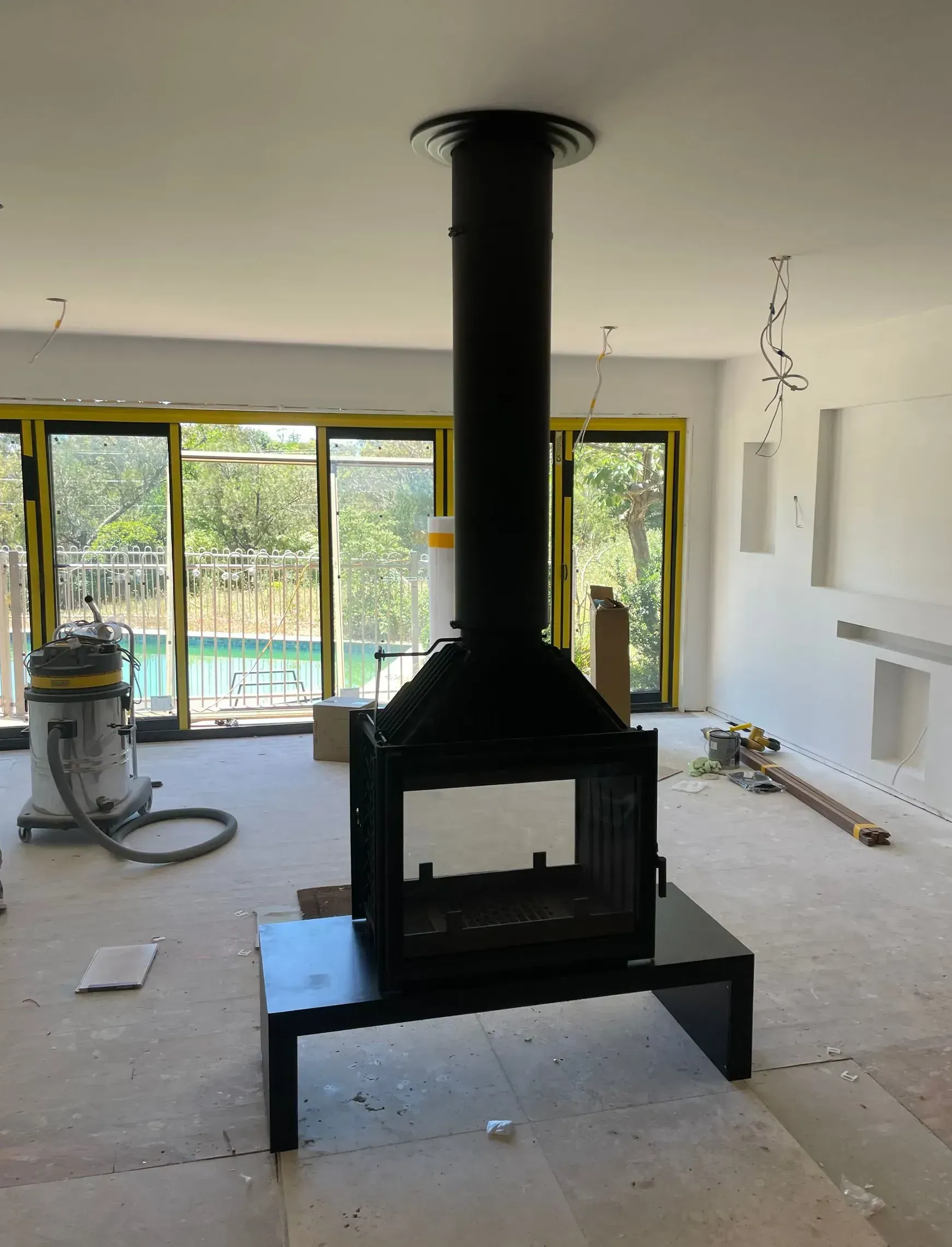 Black fireplace with chimney in a room with unfinished walls, near glass doors and a swimming pool.
