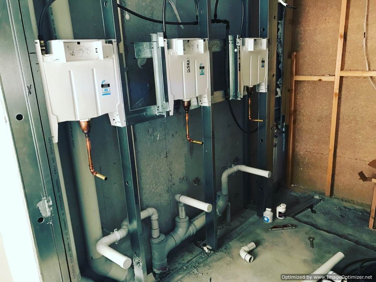 Three wall-mounted electrical boxes with copper pipes, and white PVC pipes on a construction site.