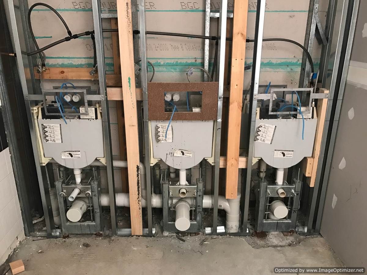 Three toilet fixtures installed within wall framing, pipes and wiring visible.