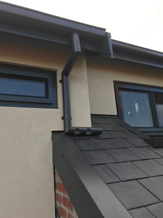 Black roof and guttering on a beige building with gray framed windows.
