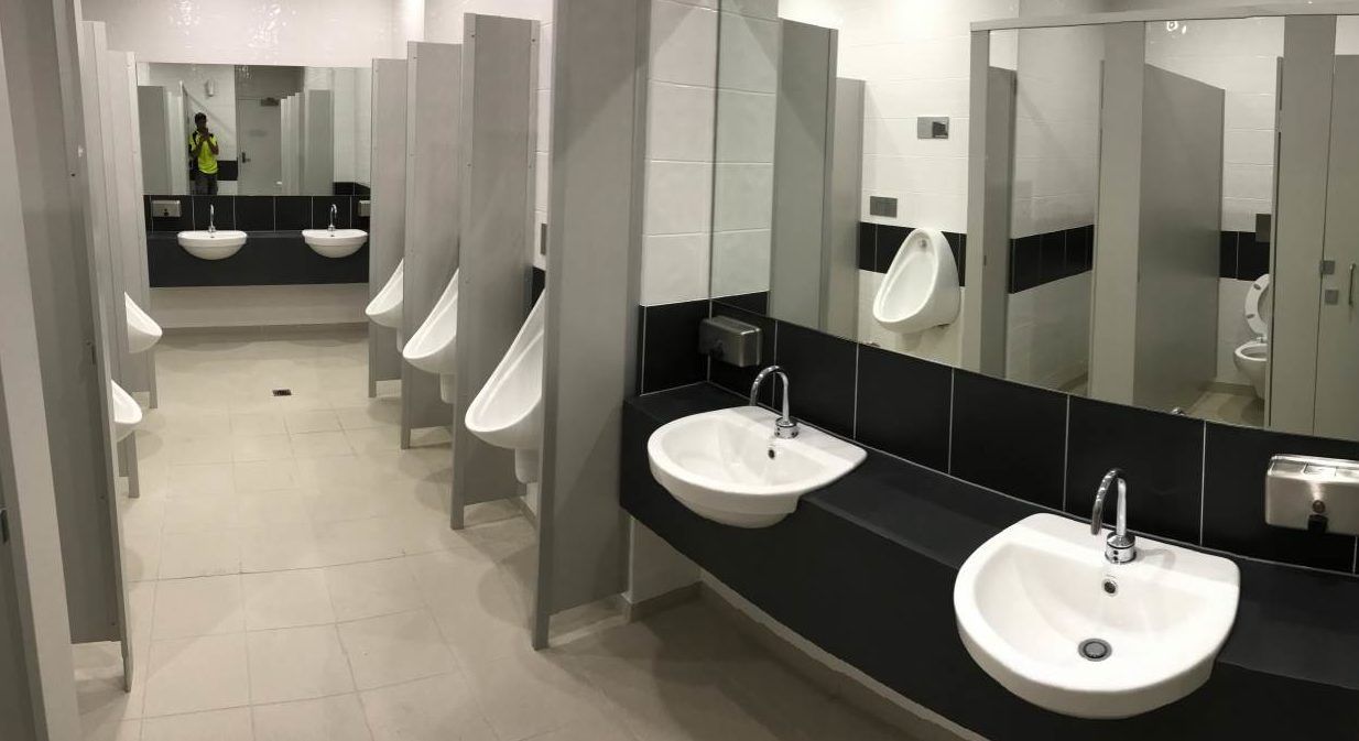 Public restroom with urinals and sinks. White and gray tones, modern design, mirrors.
