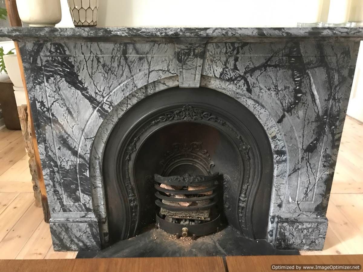 Gray and black marble fireplace with arched opening and metal grate.