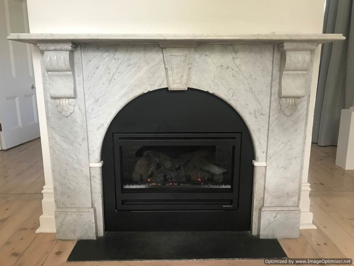 Marble fireplace with black insert in a room with hardwood floors.