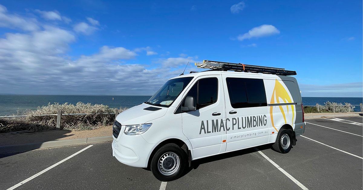 White ALMAC Plumbing van parked by the ocean on a sunny day.