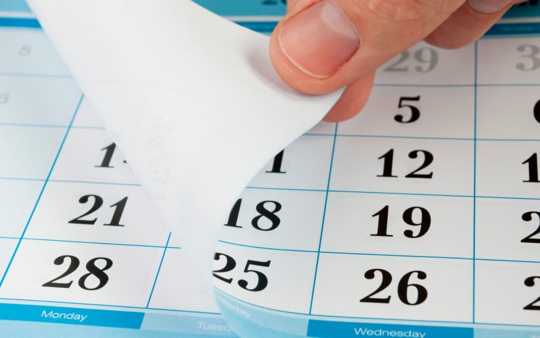 A hand peeling back a page of a calendar, revealing the date 1, with other visible dates in blue and white.