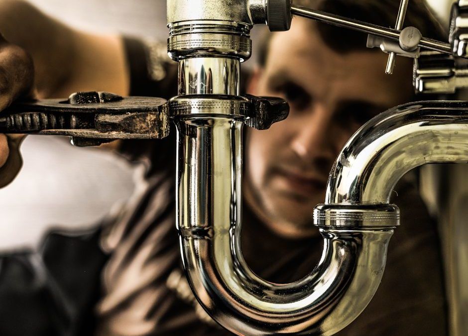 Plumber using a wrench to repair chrome plumbing pipes.
