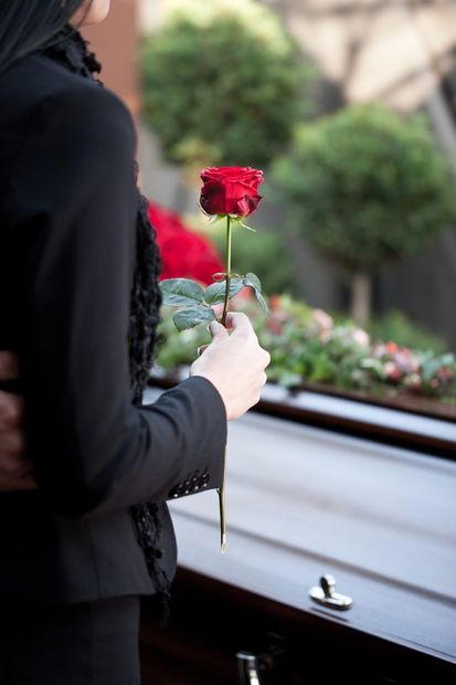 donna mentre ripone un fiore su una cassa funebre