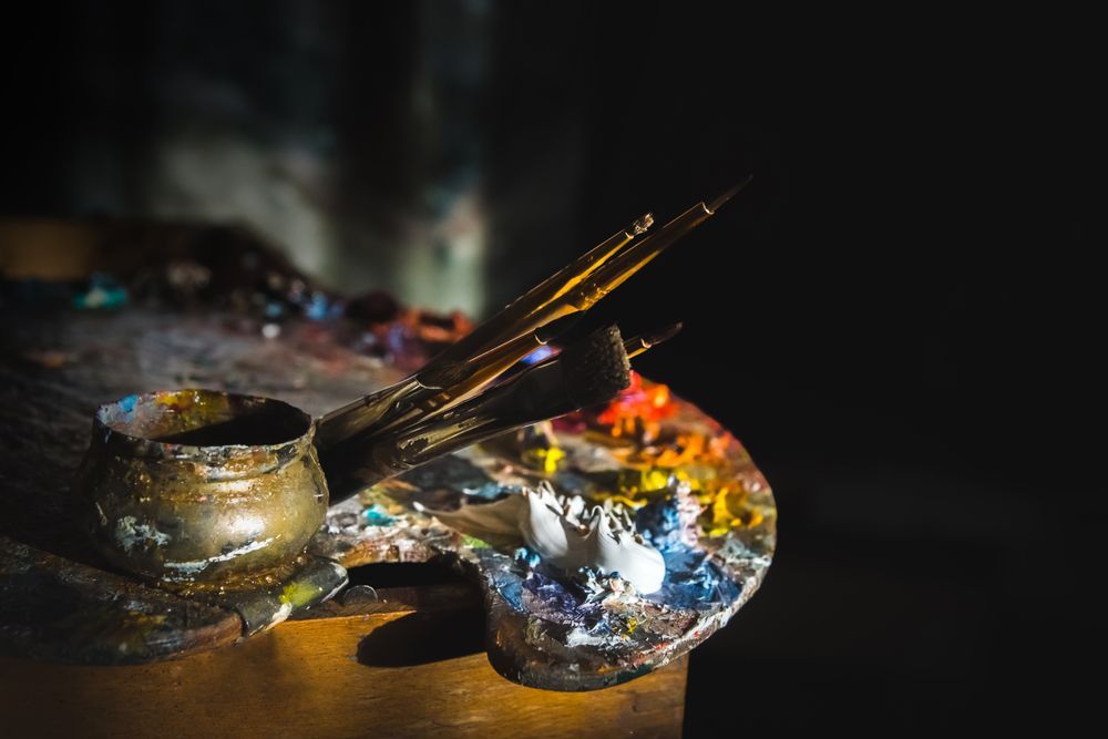 A palette of paint and brushes on a wooden table.