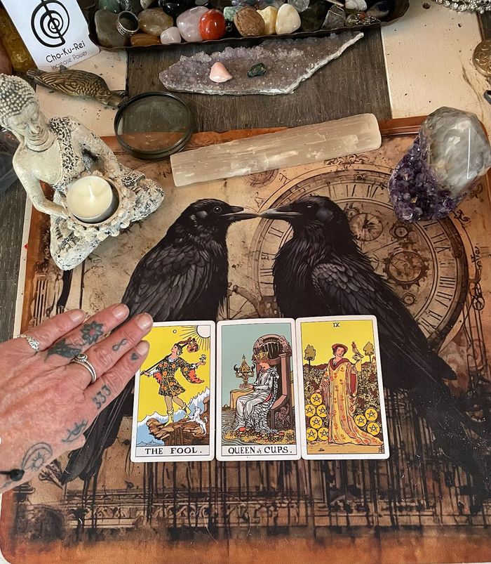 A woman is sitting at a table with tarot cards and a glass of wine.