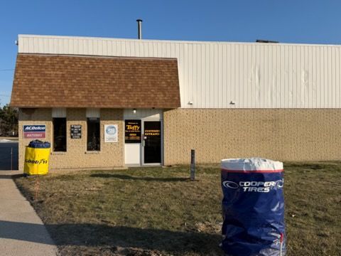 Exterior view of Rudy's Tire shop. A small brown roof covers the entrance, with blue and yellow Cooper Tire containers nearby.
