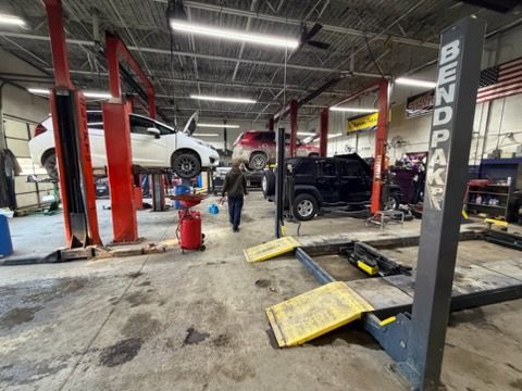 Auto repair shop interior. Several cars on lifts; one person walks through the space.