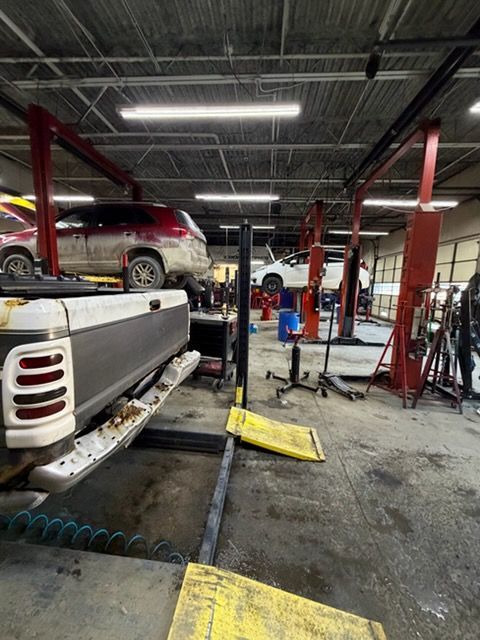 Auto repair shop with vehicles on lifts. A pickup truck is in foreground. Other cars are elevated for service.