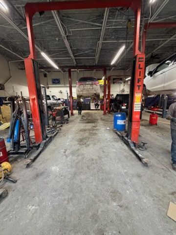 An auto repair shop with a car on a lift. Red lifts, concrete floor, tools visible.