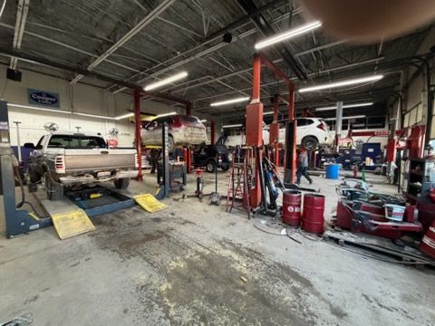 Inside a repair shop, multiple cars are lifted for service. Tools and equipment are scattered about.