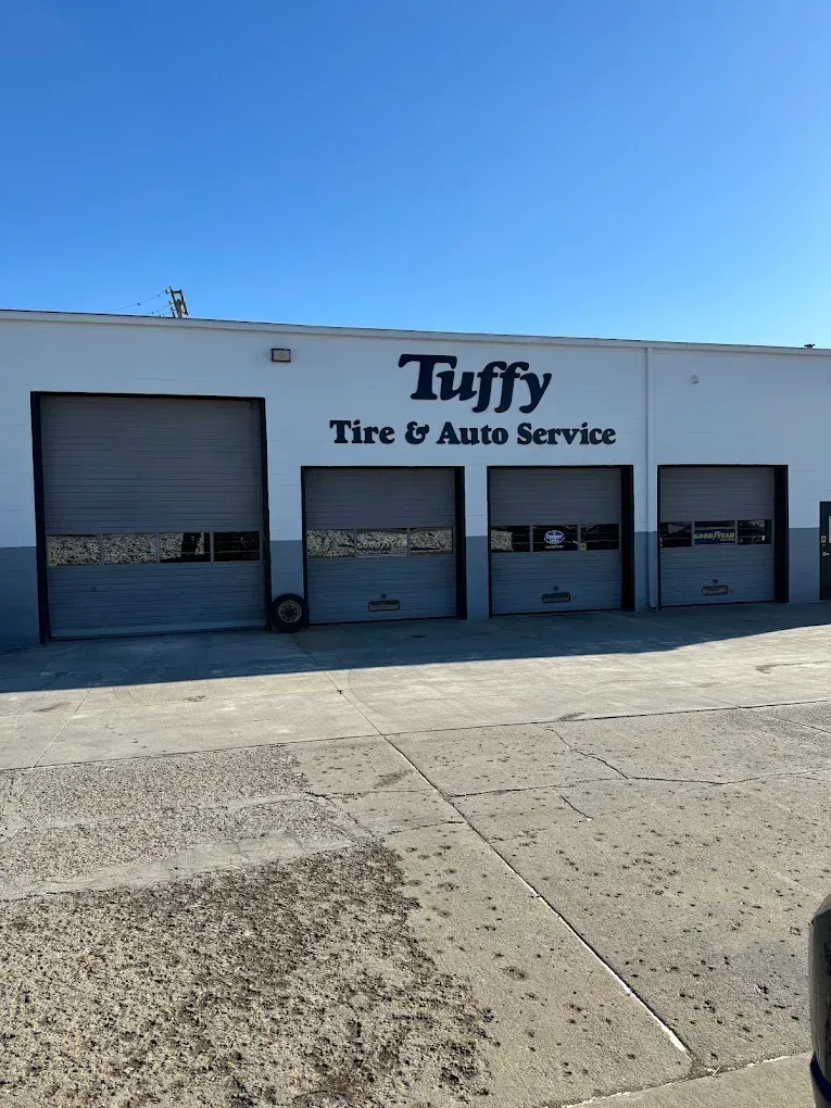 Tuffy Tire & Auto Service shop exterior with garage doors closed. Blue logo on white building under a clear sky.