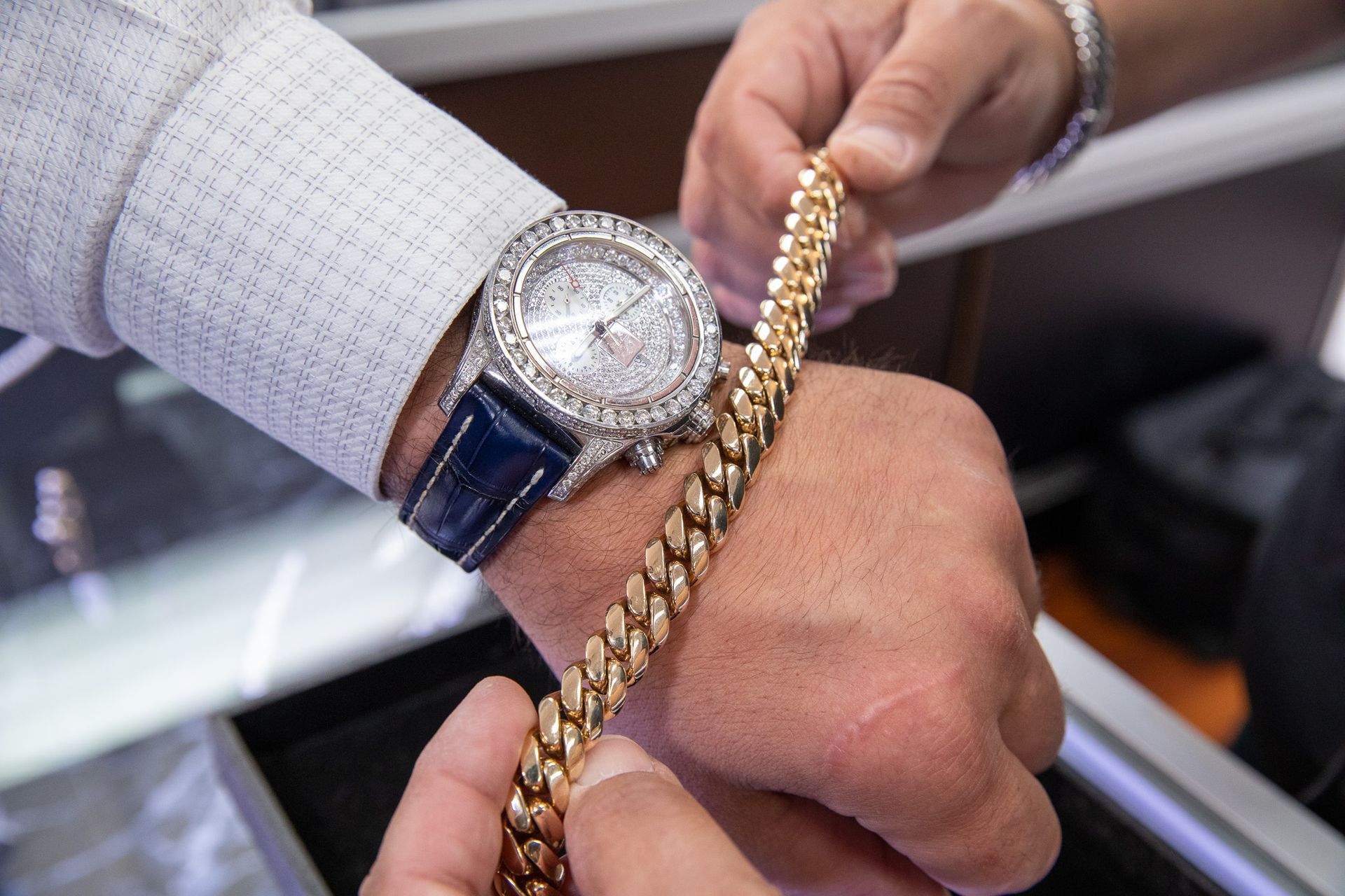 Close-up of a hand wearing a luxury watch and holding a gold chain bracelet.
