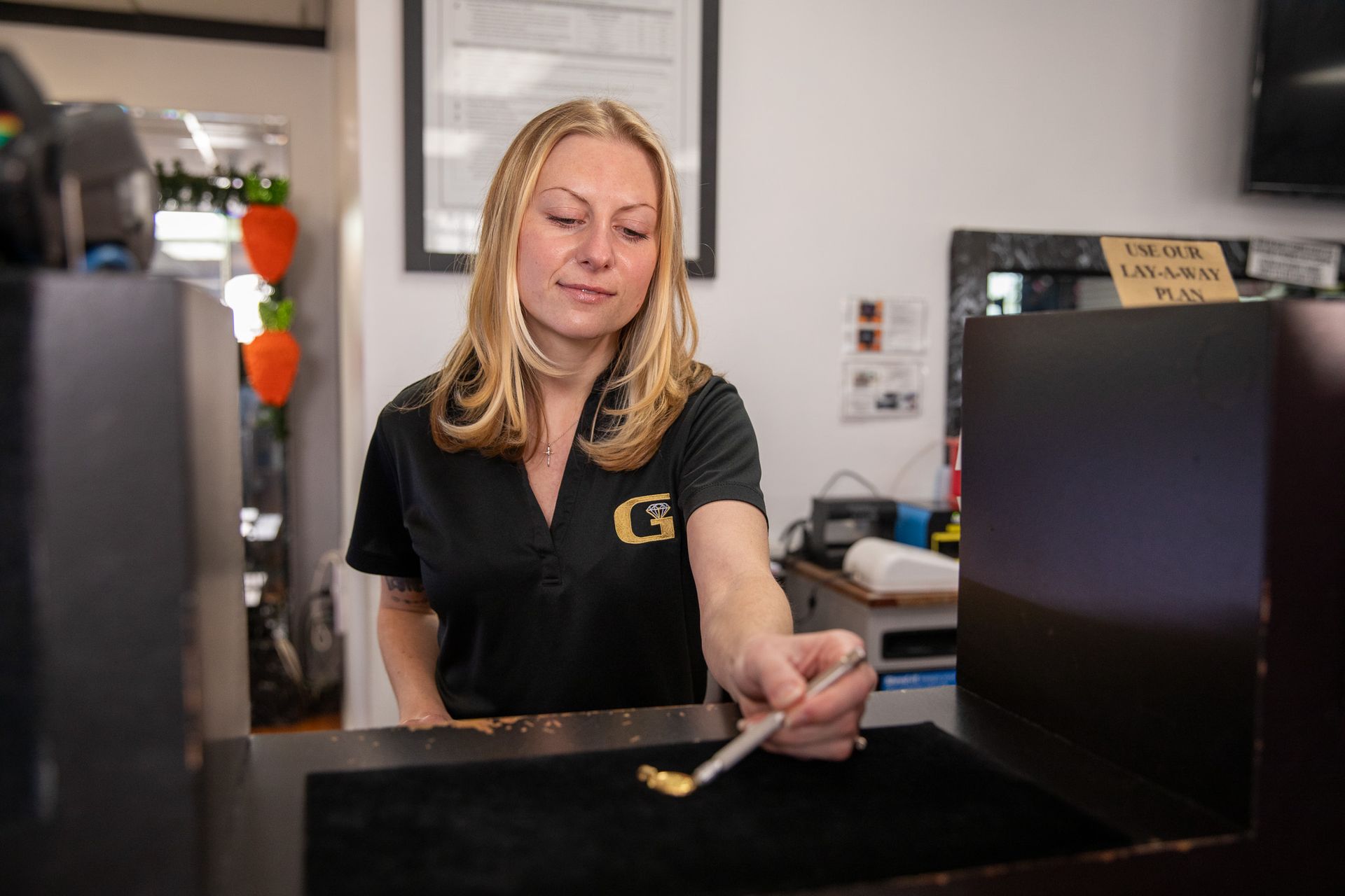 Woman in black shirt examining gold item with a tool at a shop counter.