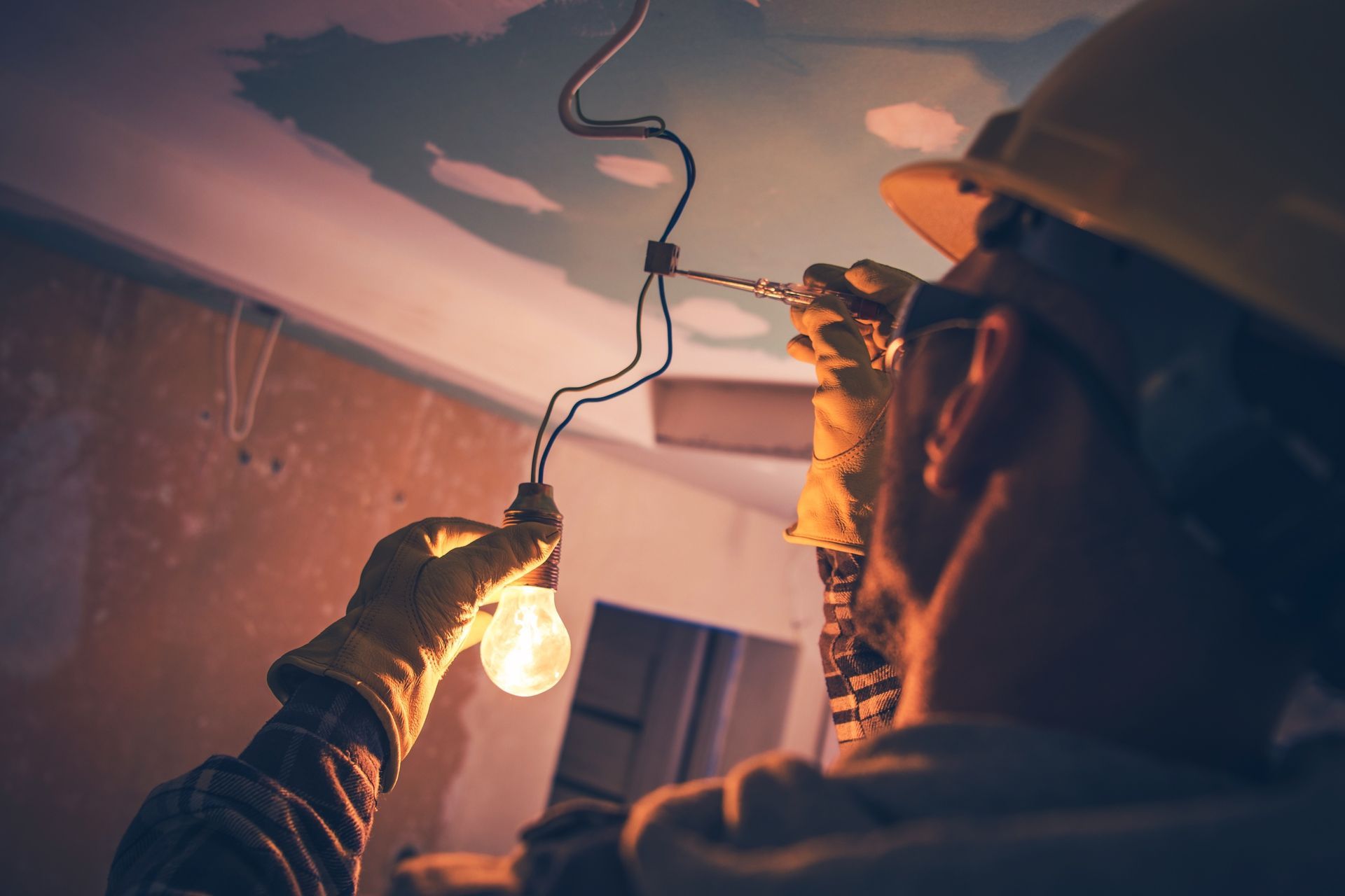 Electrician wiring a hanging light bulb from the ceiling during interior renovation.