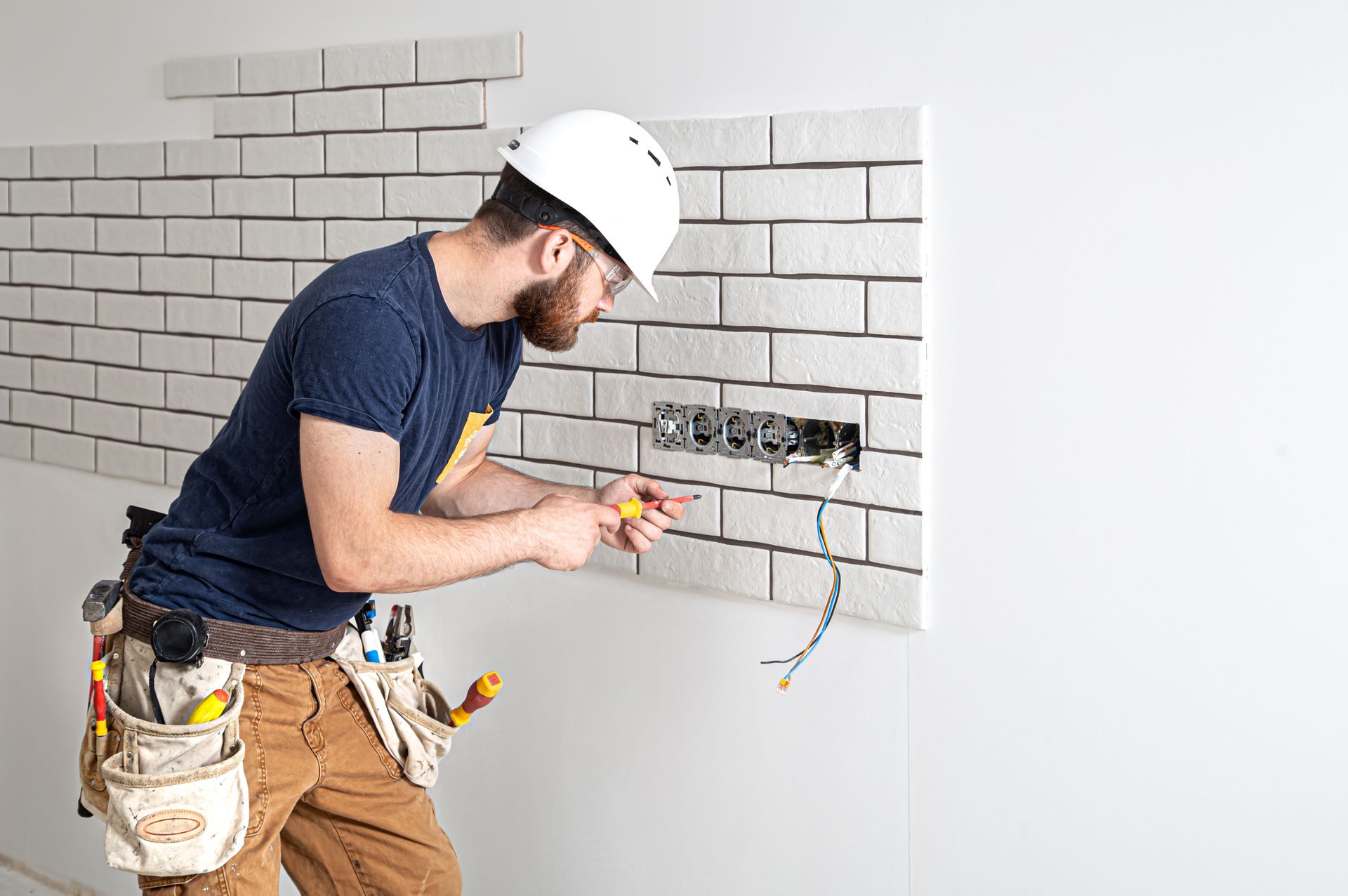 A skilled electrician wiring a brick wall outlet, offering professional electrician services.