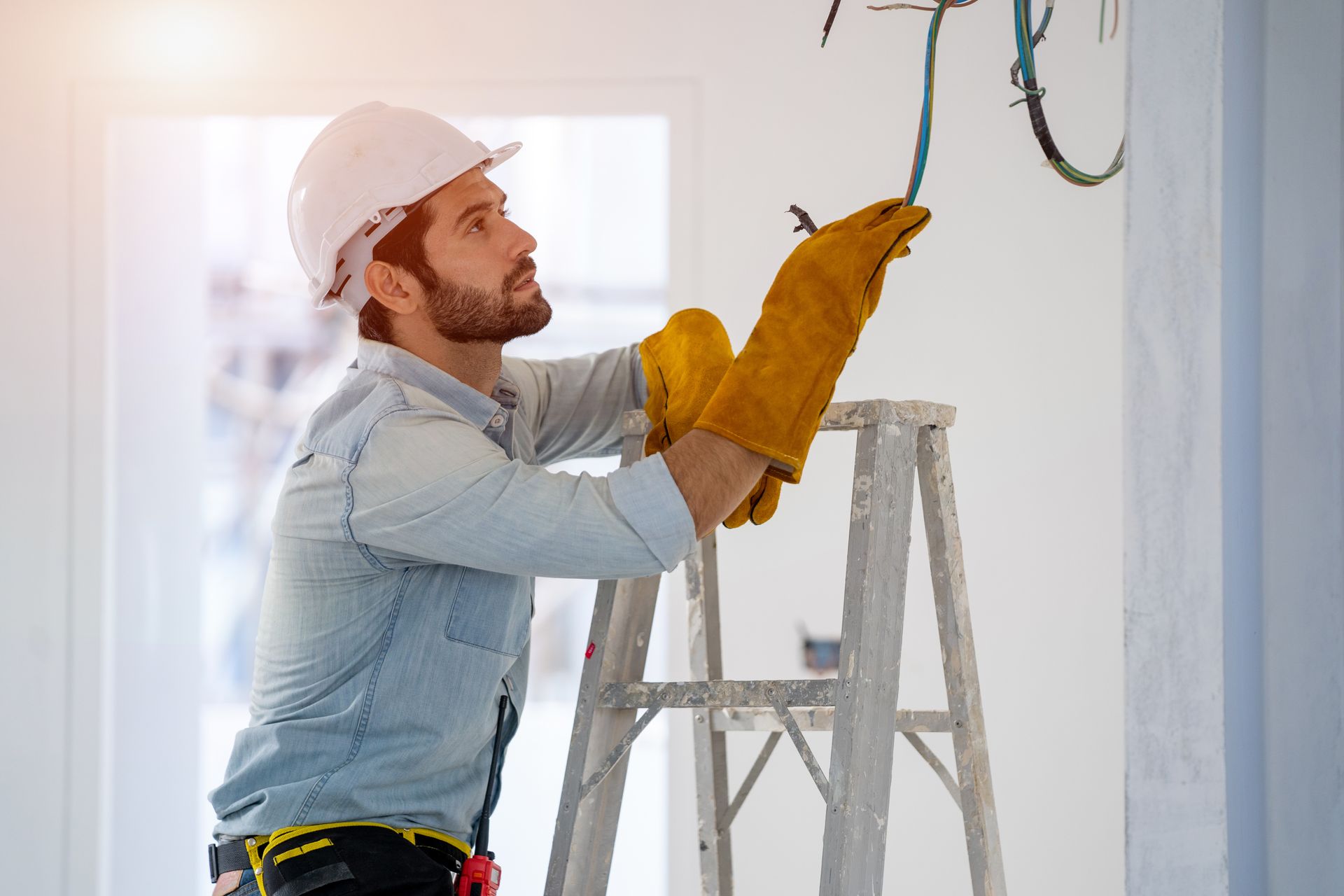 A technician performing commercial electrical repair while working on exposed wiring from a ladder.