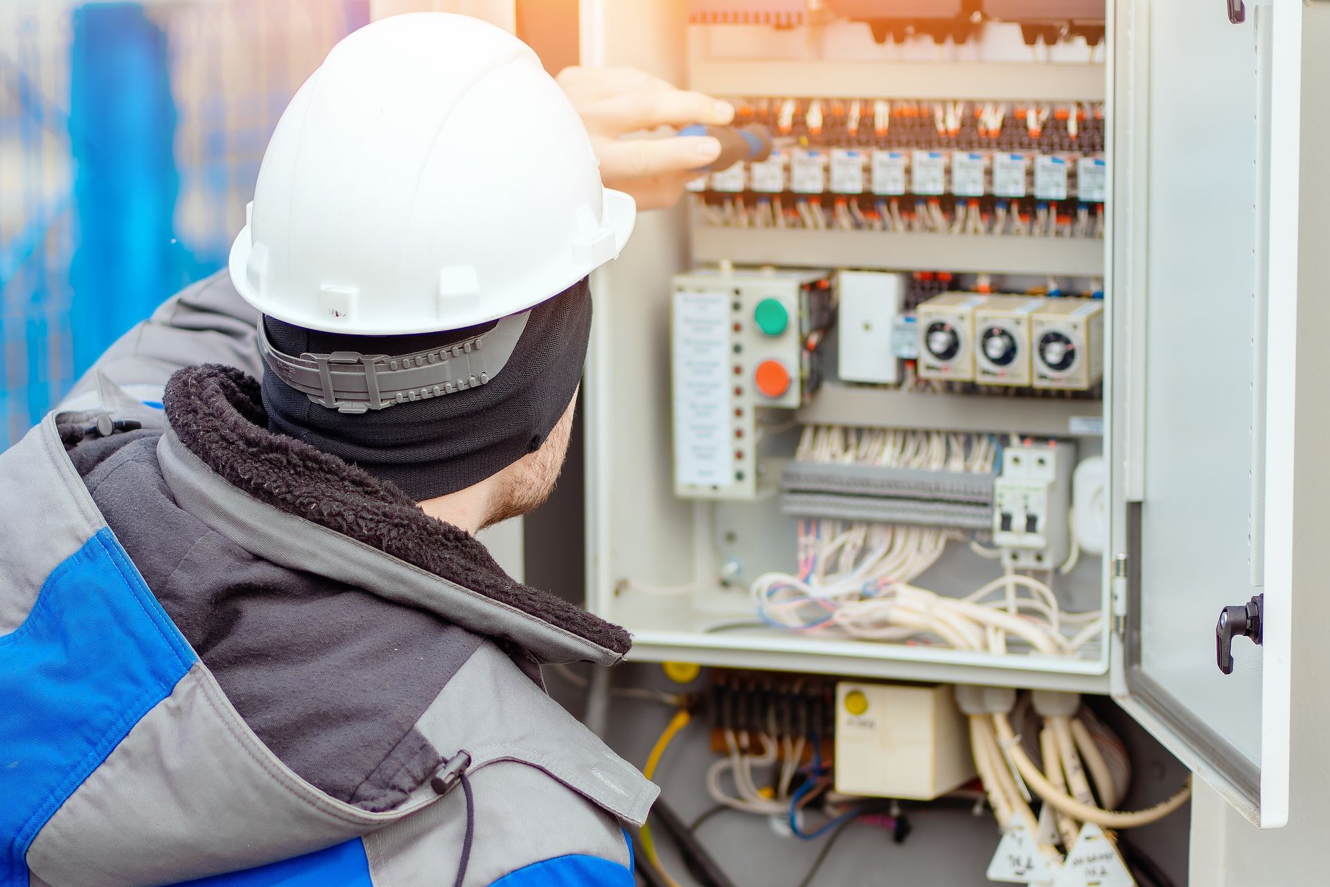 Electrician in white hard hat providing electrical services at a control panel outside.