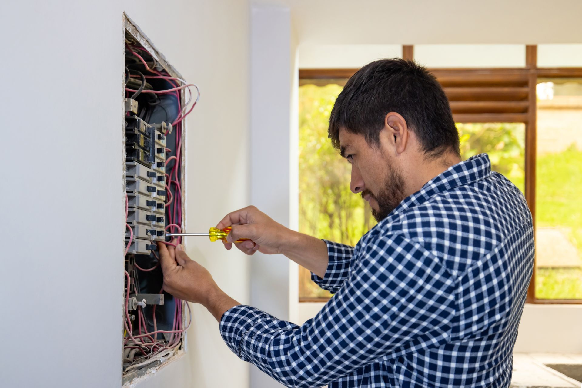 Electrician fixing a fuse box at a house and using a screwdriver.