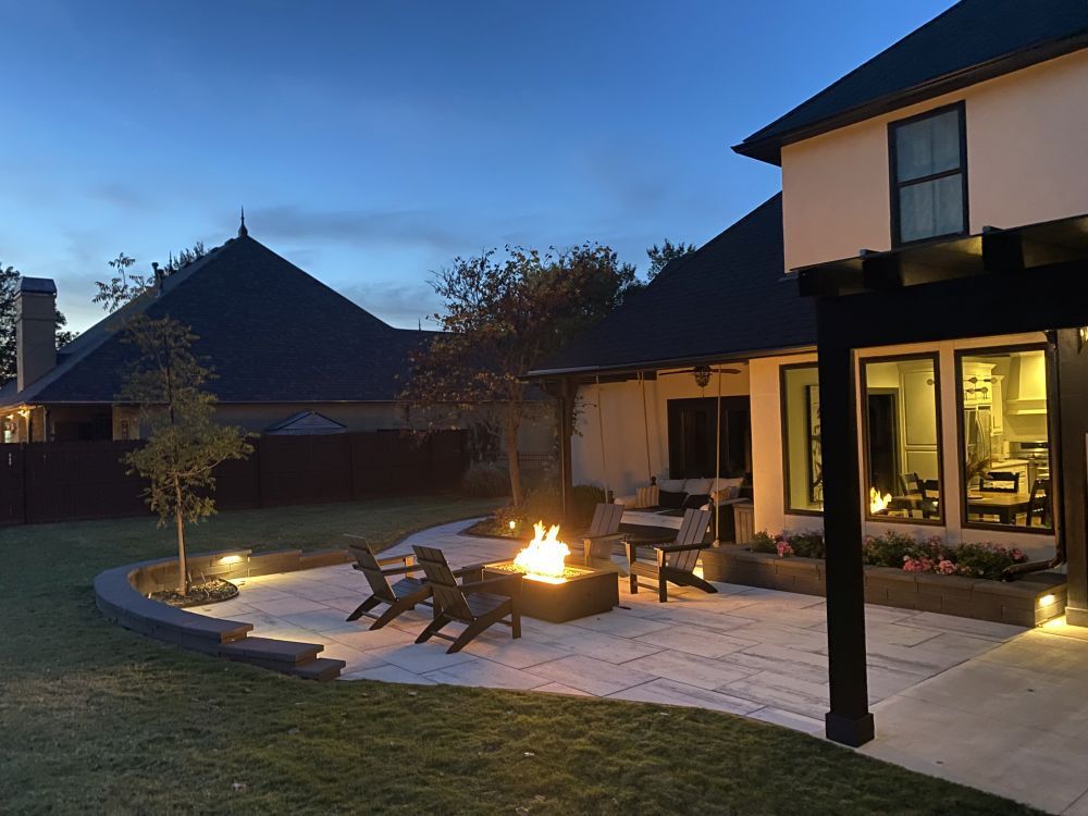 Backyard patio at dusk with fire pit, lounge chairs, and warm lights by a house