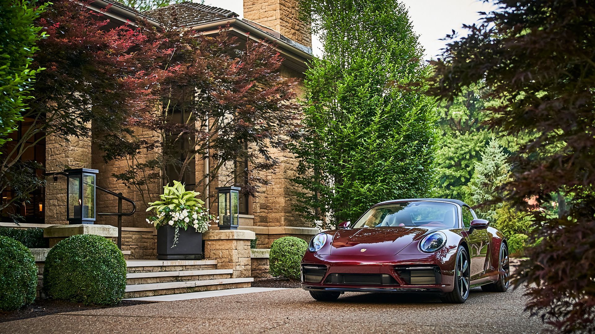 A red porsche 911 is parked in front of a brick house.