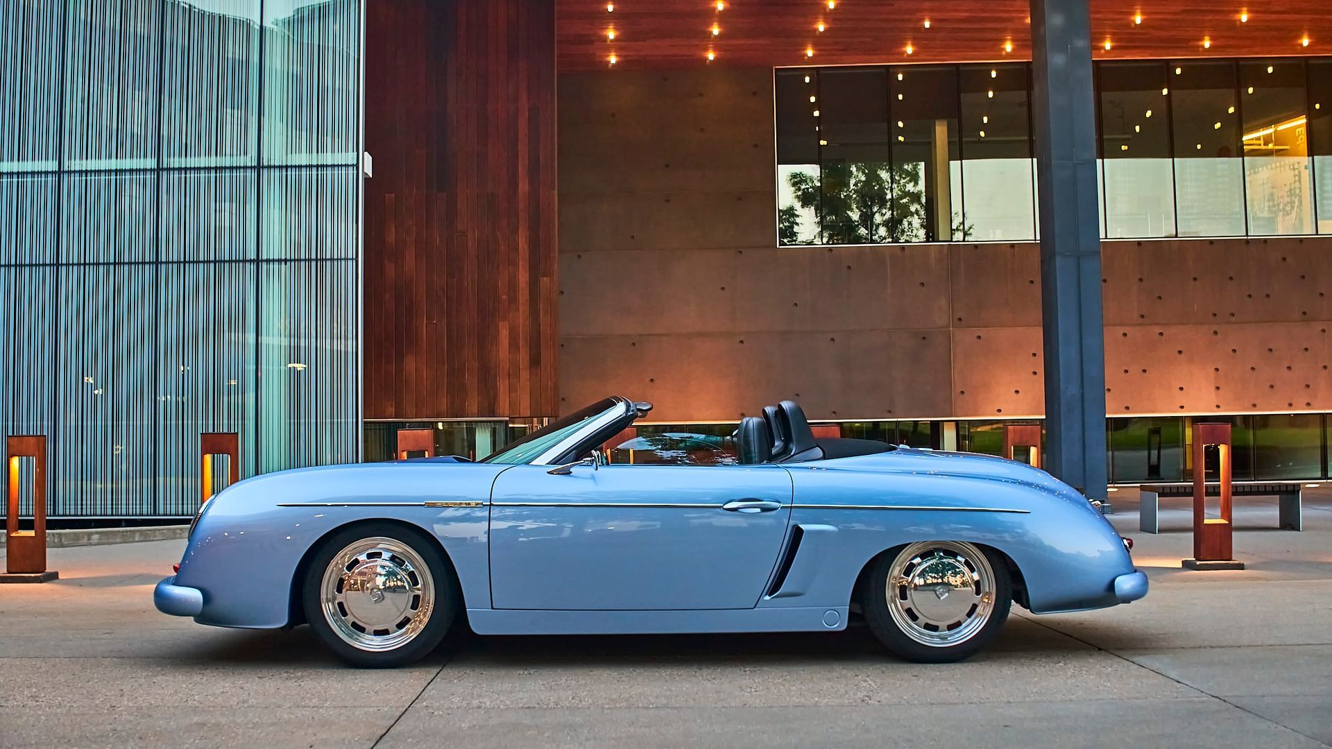 Light blue vintage convertible parked in front of a modern building with glass and wood paneling.
