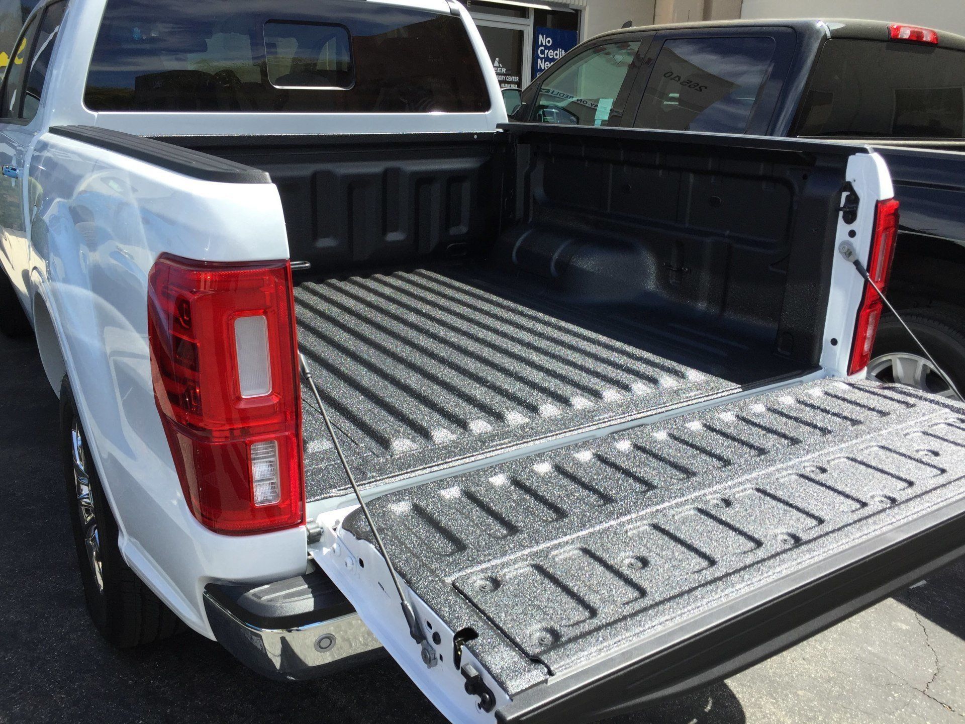 White pickup truck bed, open tailgate. Black protective liner. Tail light visible.