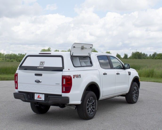 Truck bed toppers stacked on metal racks, various colors, outdoor setting.