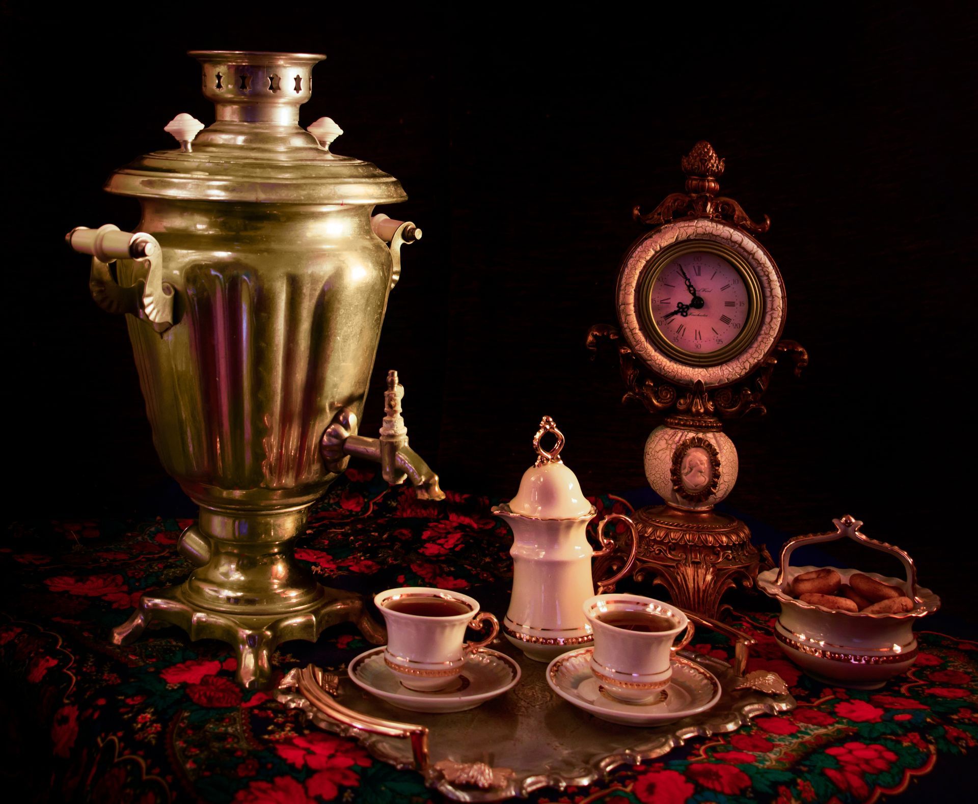 A samovar and a clock are on a table with cups of tea