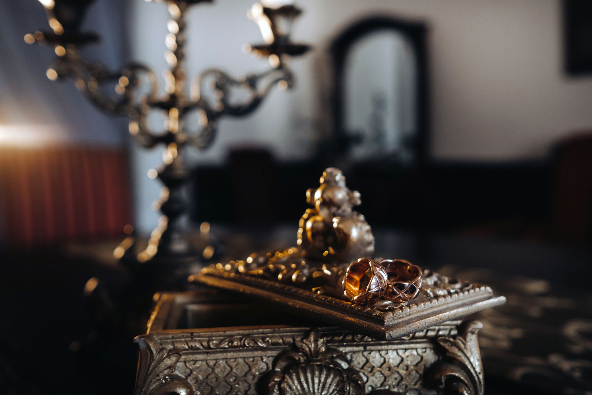 A close up of a jewelry box with a candle holder in the background.