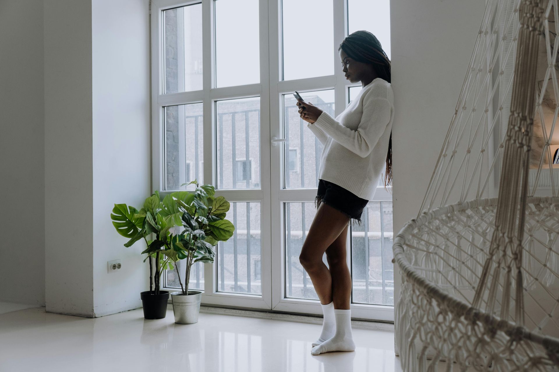 A woman is standing in a hallway looking at her cell phone.