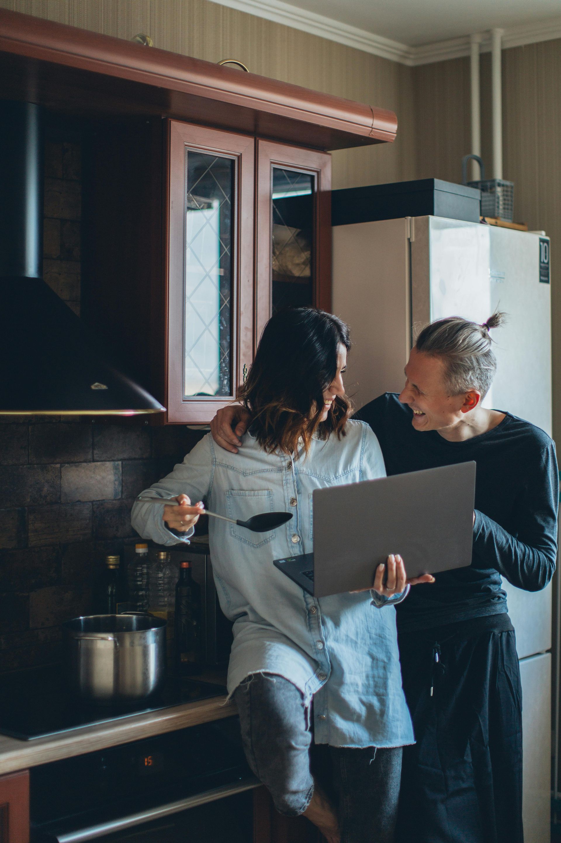 A man and a woman are looking at a laptop computer in a kitchen.